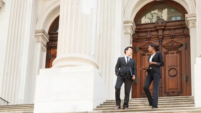 Man and woman dressed in suits walking down steps of a courthouse building